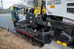 Road construction worker operating Roadtec asphalt paving machine on roadside