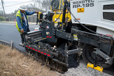 Road construction worker operating Roadtec asphalt paving machine on roadside