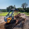 Yellow Hyundai tracked skid steer loader moving dirt on a construction site with green field background
