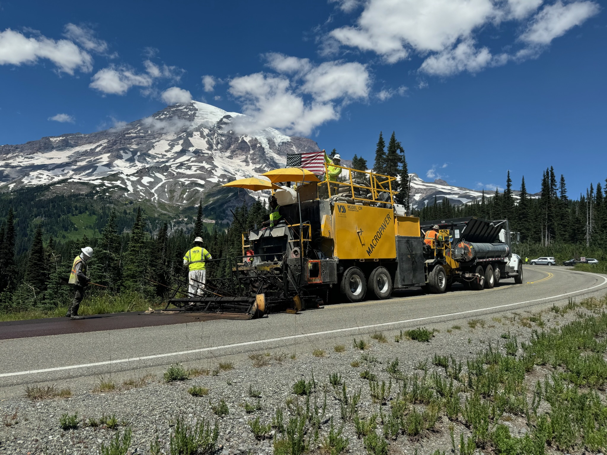Yellow road paving machine working on highway near snow-capped Mount Rainier
