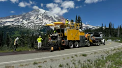 Yellow road paving machine working on highway near snow-capped Mount Rainier