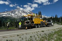Yellow road paving machine working on highway near snow-capped Mount Rainier