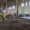 Construction workers in safety gear inside large industrial building with dirt floor