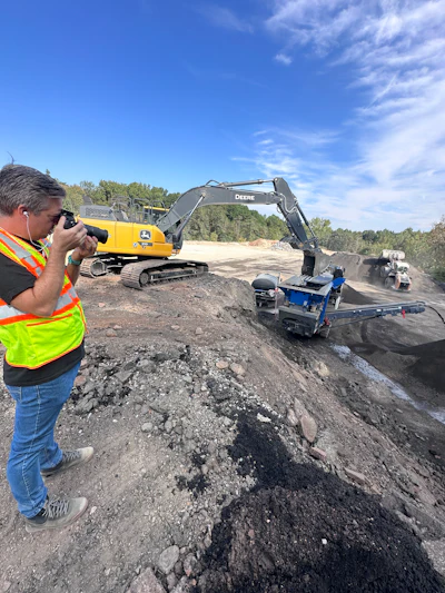 Construction site with yellow John Deere excavator processing materials near trees