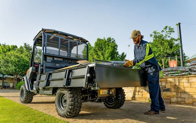 Utility work vehicle with worker in safety vest unloading equipment outdoors