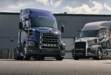 Two Mack semi-trucks parked side by side in industrial loading area