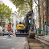 Yellow excavator digging street with construction worker in orange safety vest
