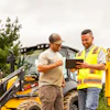 Construction workers reviewing tablet near yellow excavator and heavy machinery
