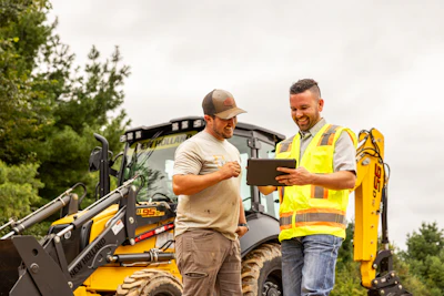 Construction workers reviewing tablet near yellow excavator and heavy machinery