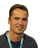 Professional headshot of a smiling person wearing a striped shirt and teal lanyard Headshot