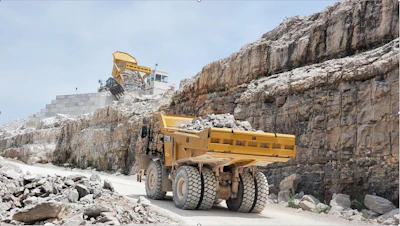 Yellow dump truck hauling rocks in limestone quarry with steep rocky cliff walls