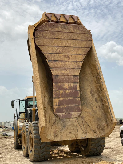 Large yellow dump truck with raised cargo bed on dusty construction site