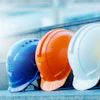 Four construction safety helmets in blue, orange, white, and yellow on a blurred background