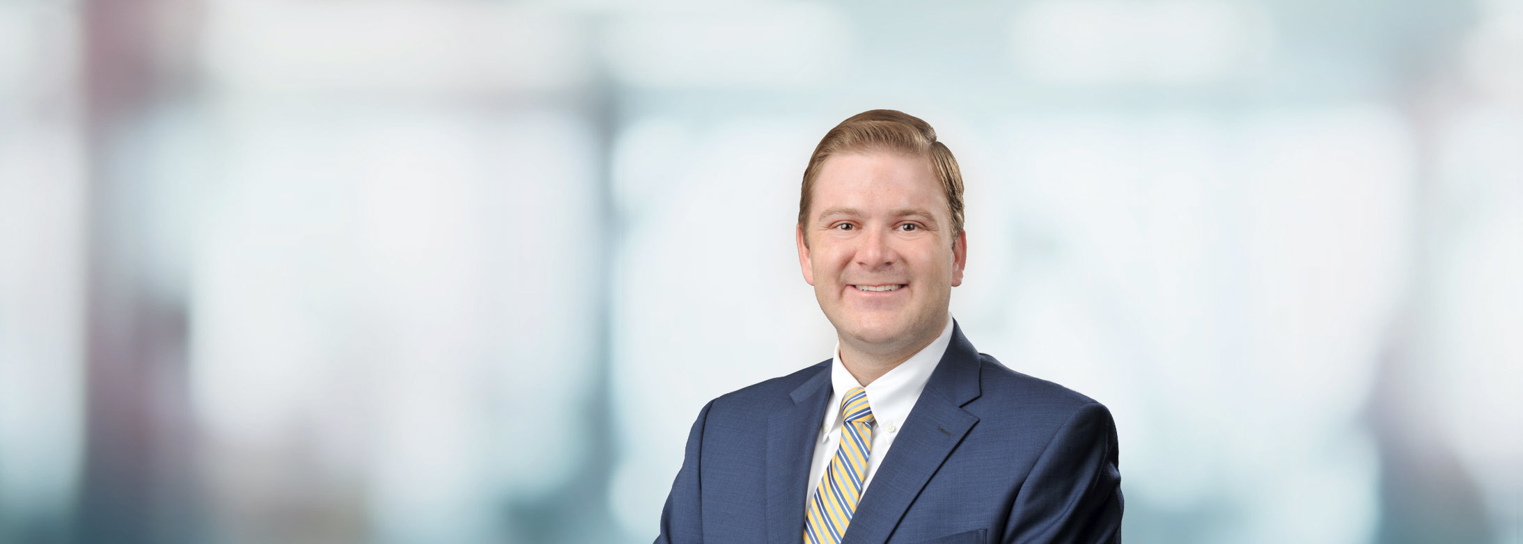 Smiling professional in navy blue suit and striped tie against blurred background Headshot