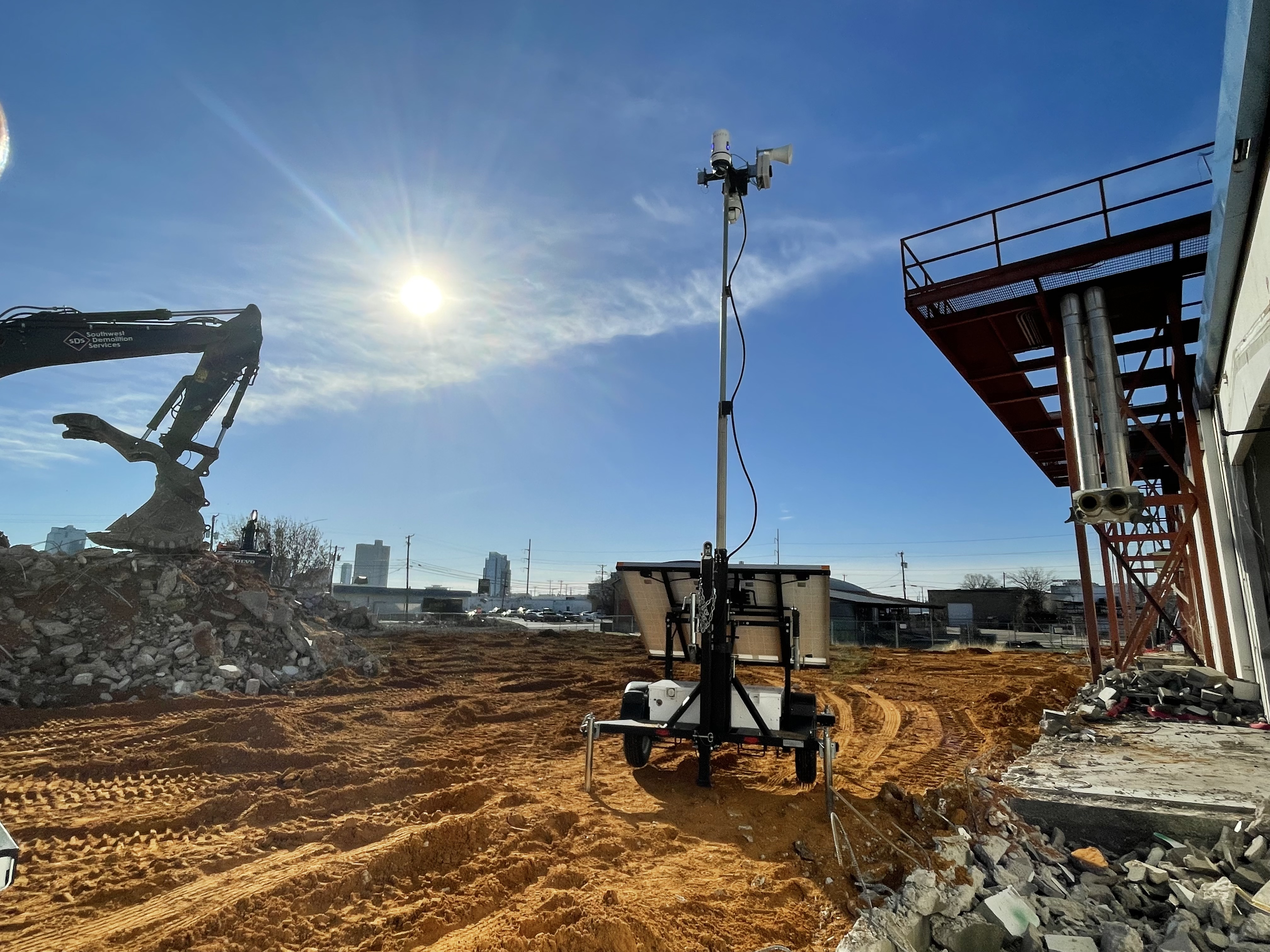 Construction site with excavator, solar tower, and sandy ground under bright blue sky