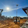 Construction site with excavator, solar tower, and sandy ground under bright blue sky
