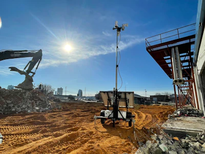 Construction site with excavator, solar tower, and sandy ground under bright blue sky