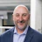 Smiling professional in navy blazer and checked shirt, bald with gray beard Headshot