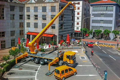 Yellow crane truck parked on urban street with red vehicles and surrounding buildings
