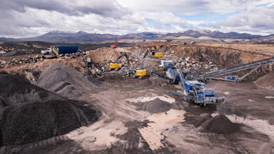 Mining quarry with blue and yellow excavators processing rocky terrain, mountain landscape background