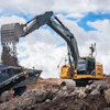 Yellow John Deere excavator loading rocks at construction site with cloudy sky