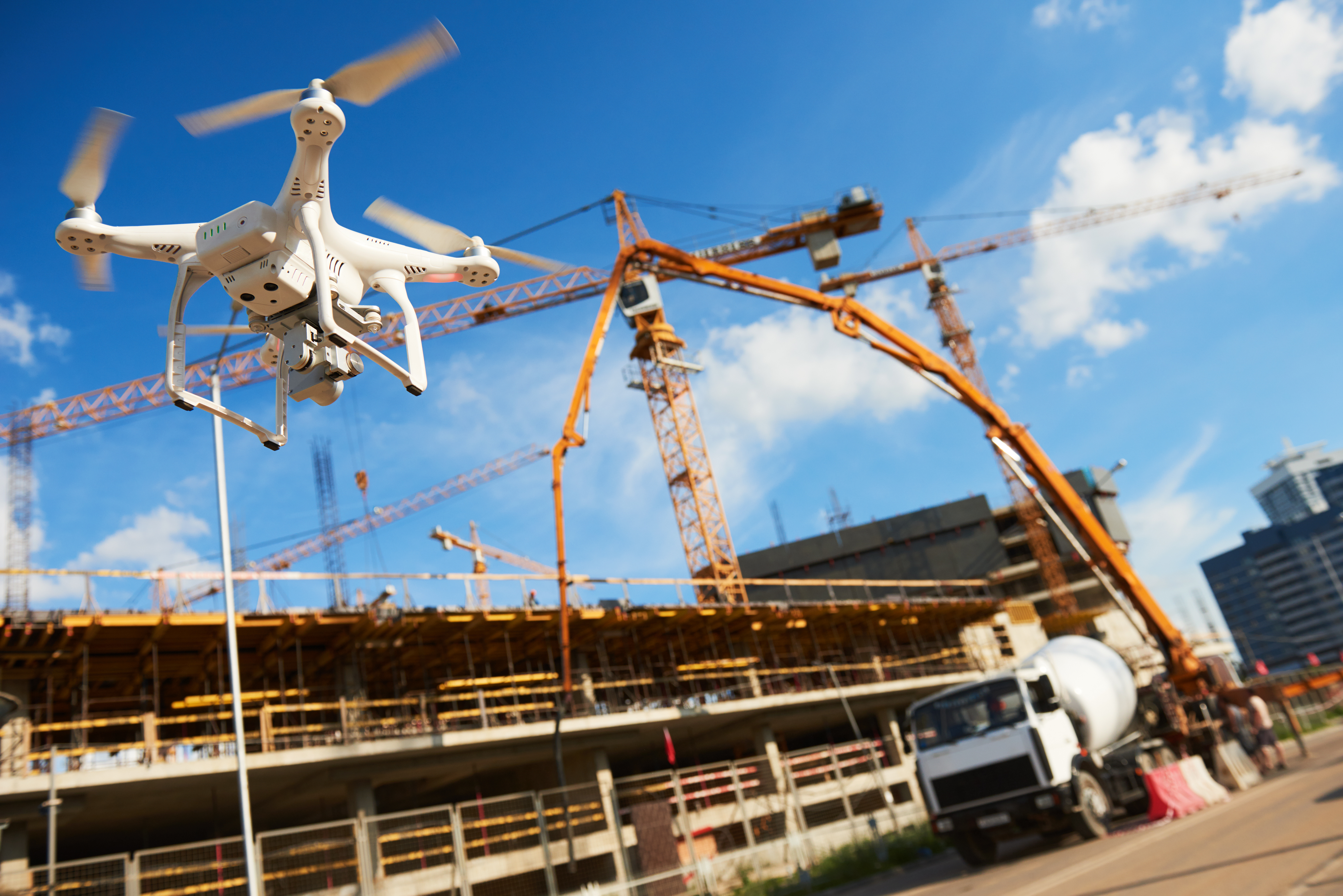White drone hovering near construction site with yellow cranes and concrete mixer