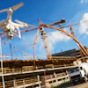 White drone hovering near construction site with yellow cranes and concrete mixer