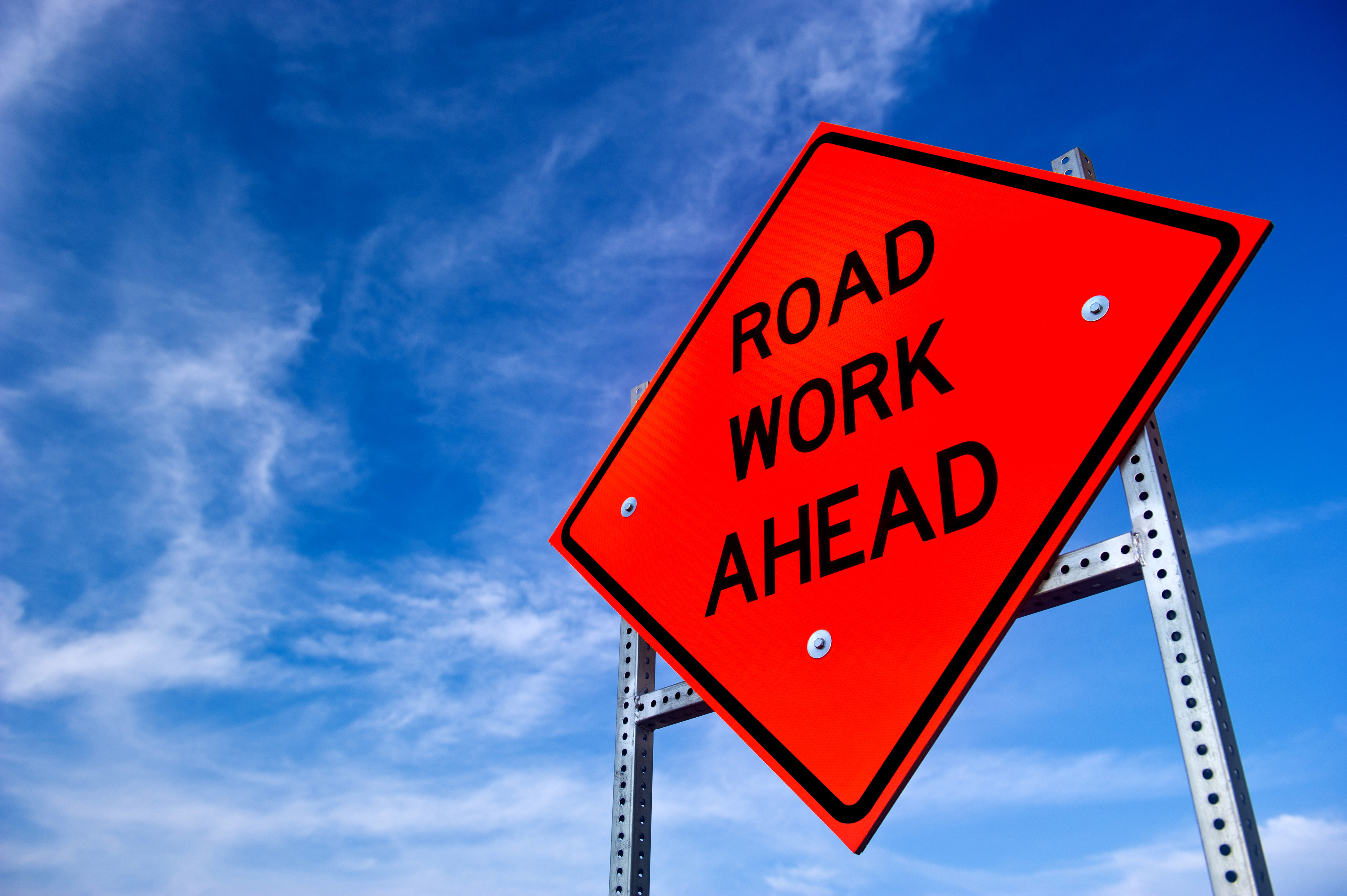 Bright red Road Work Ahead sign against a blue sky with wispy clouds