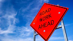 Bright red Road Work Ahead sign against a blue sky with wispy clouds