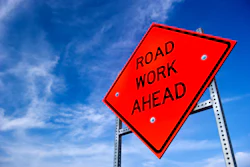 Bright red Road Work Ahead sign against a blue sky with wispy clouds