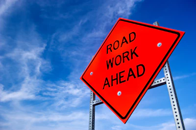 Bright red Road Work Ahead sign against a blue sky with wispy clouds