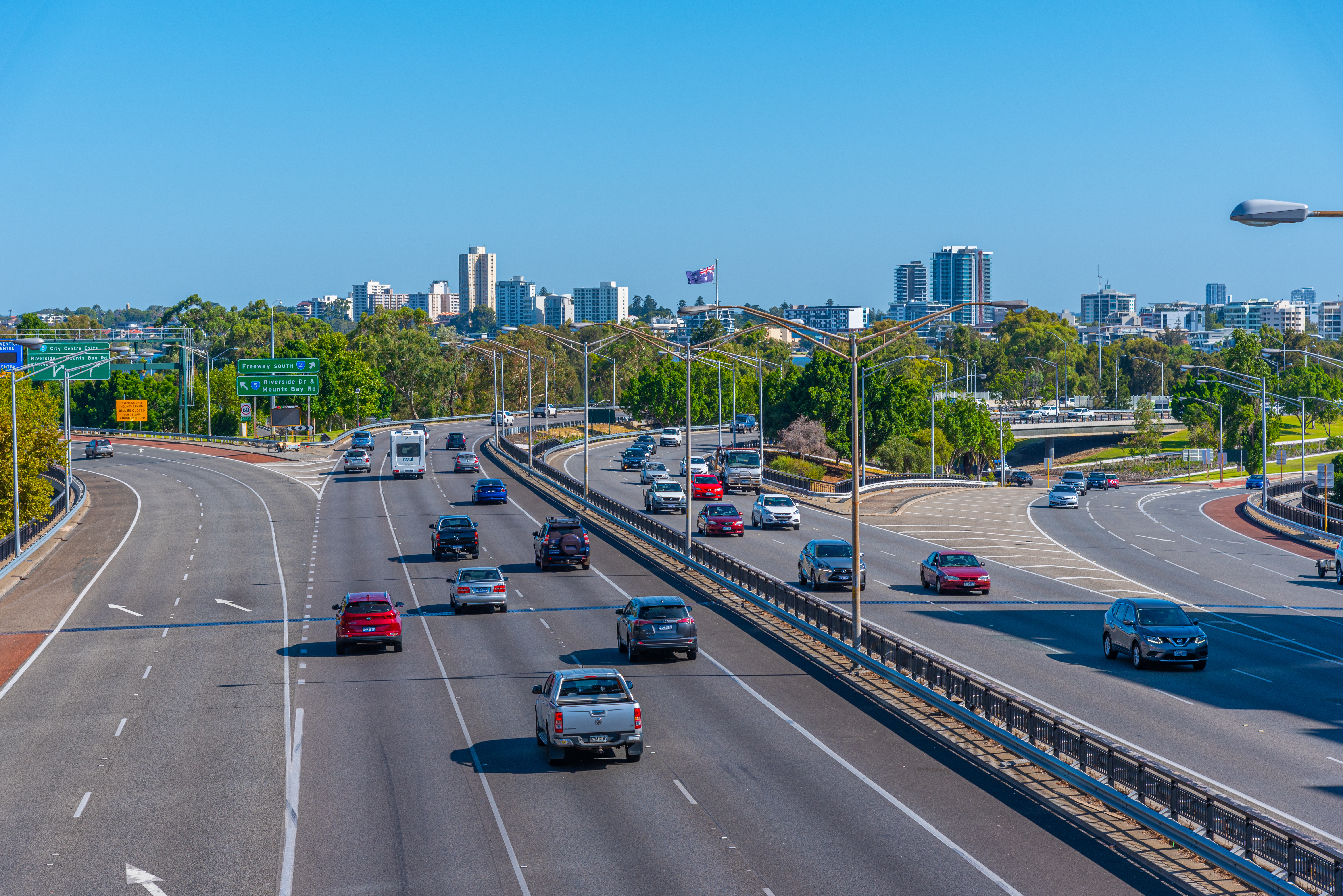 Multi-lane urban highway with vehicles, curving roadway and city skyline under blue sky