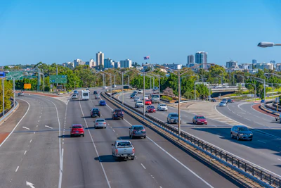 Multi-lane urban highway with vehicles, curving roadway and city skyline under blue sky