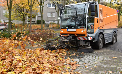 Orange street sweeper clearing fallen autumn leaves on cobblestone street