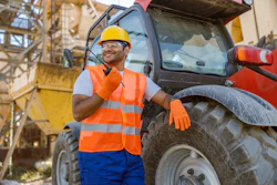 Construction worker in yellow hard hat and orange safety vest standing near red tractor