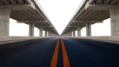 Symmetrical highway under concrete bridge with orange center line converging to vanishing point