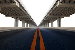Symmetrical highway under concrete bridge with orange center line converging to vanishing point