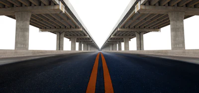 Symmetrical highway under concrete bridge with orange center line converging to vanishing point