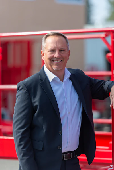 Smiling businessman in black suit standing near red industrial equipment