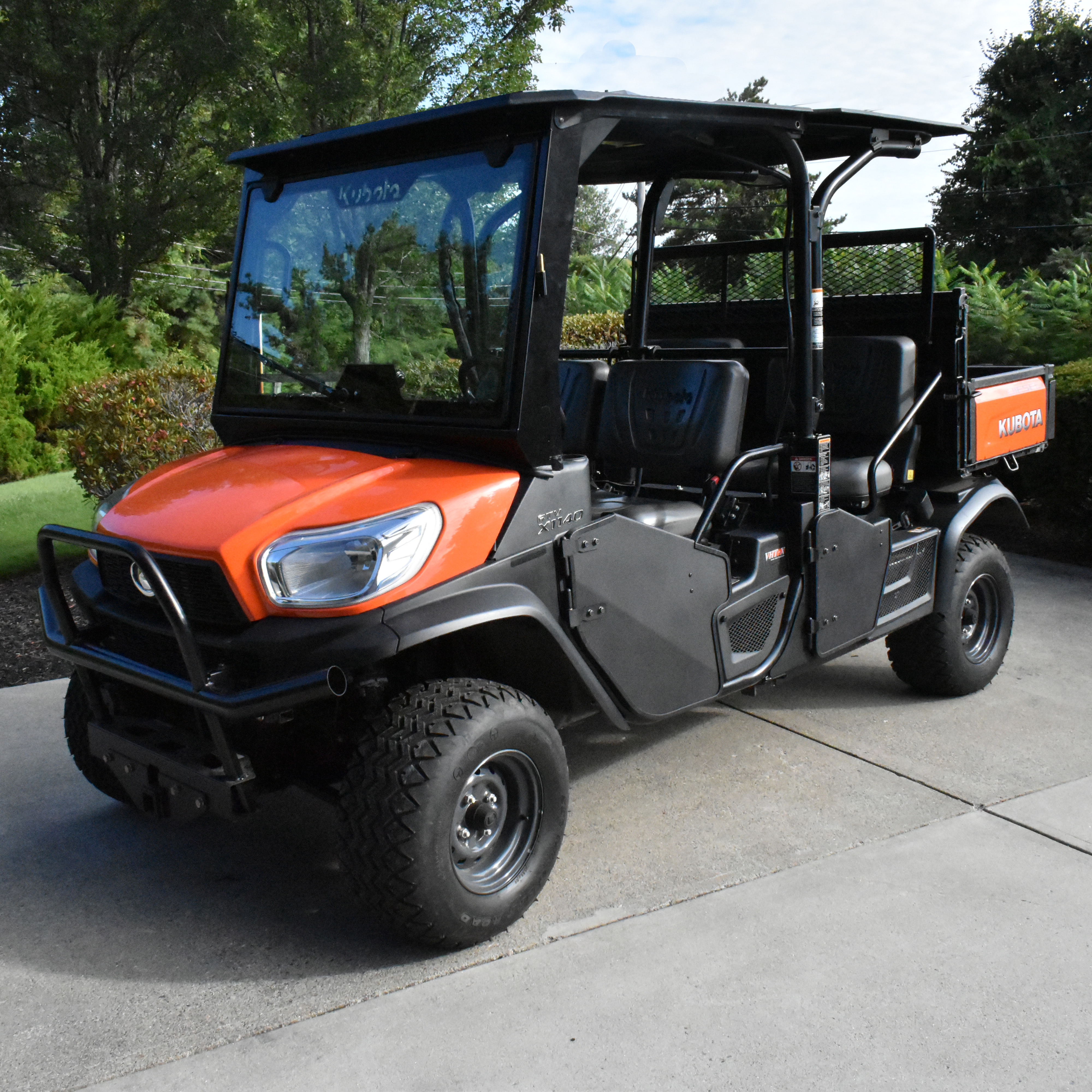 Orange Kubota utility vehicle parked on concrete with trees in background