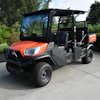 Orange Kubota utility vehicle parked on concrete with trees in background