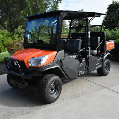 Orange Kubota utility vehicle parked on concrete with trees in background