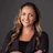 Professional woman smiling in black blazer against gray background Headshot