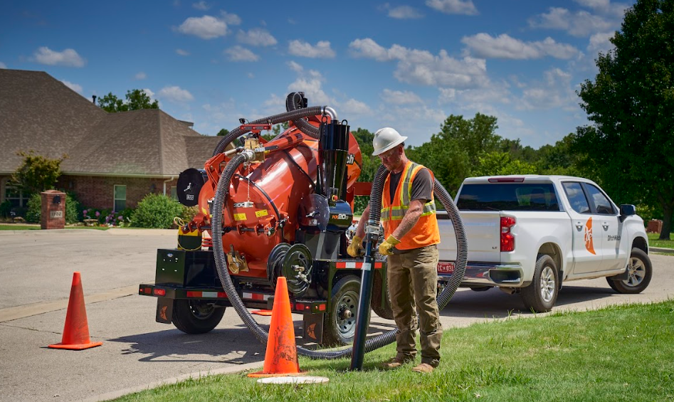 Construction worker operating vacuum truck with safety cones near residential area