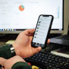 Hand holding smartphone with messaging app, laptop and data chart in background