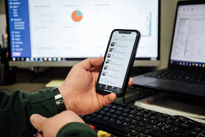 Hand holding smartphone with messaging app, laptop and data chart in background