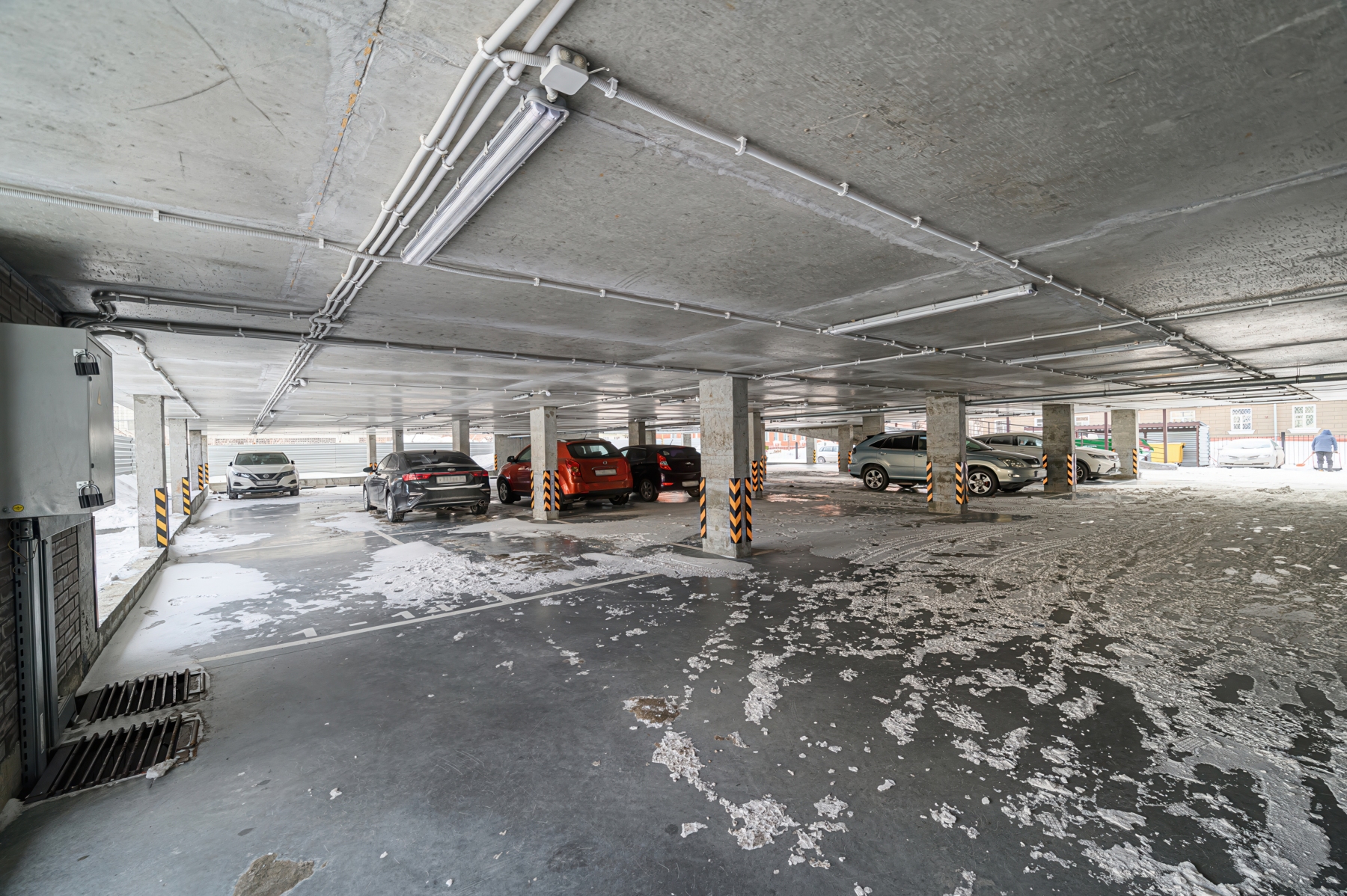 Underground parking garage with several vehicles parked near concrete pillars and exposed ceiling pipes
