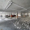 Underground parking garage with several vehicles parked near concrete pillars and exposed ceiling pipes