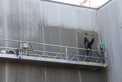 Two construction workers on suspended scaffolding inspecting industrial metal wall