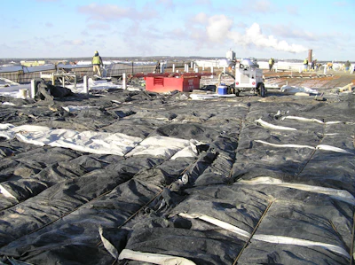 Construction site with black and white geotextile fabric, workers in safety gear, and red equipment